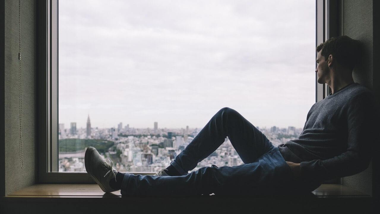 Man sitting on a nook in the window overlooking the city