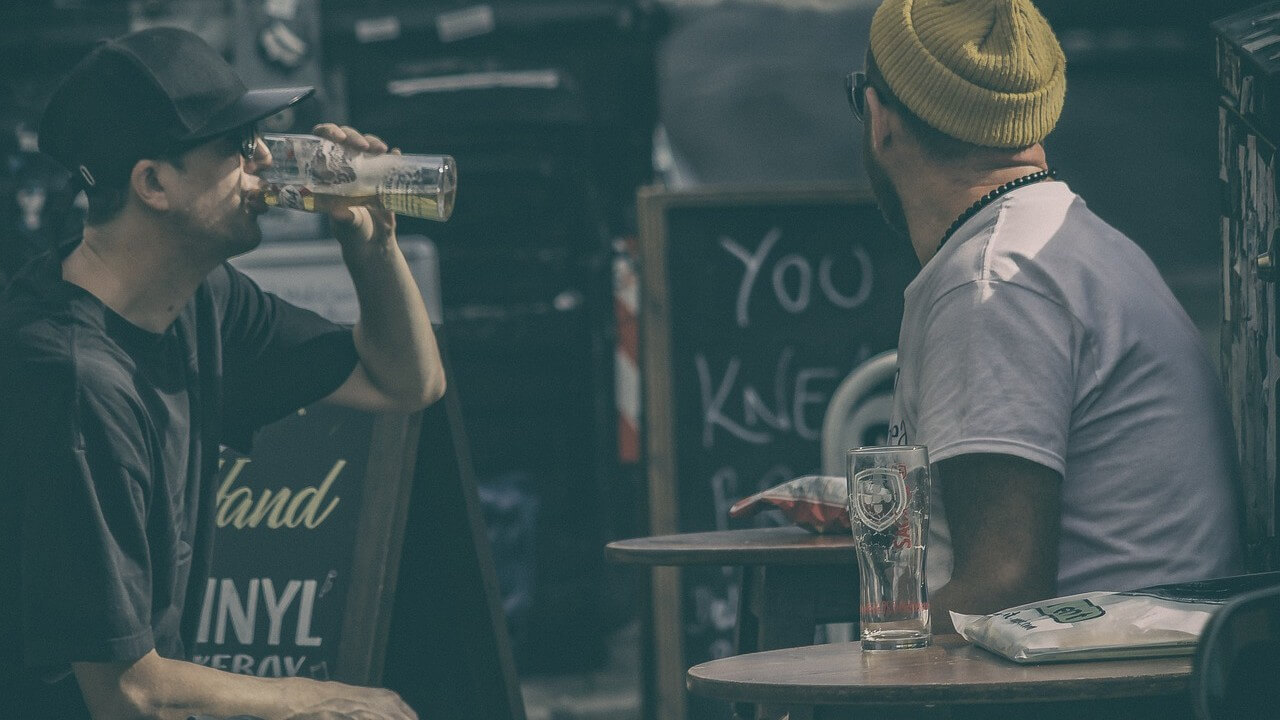 Two men sitting in a bar and one of them is drinking a beer