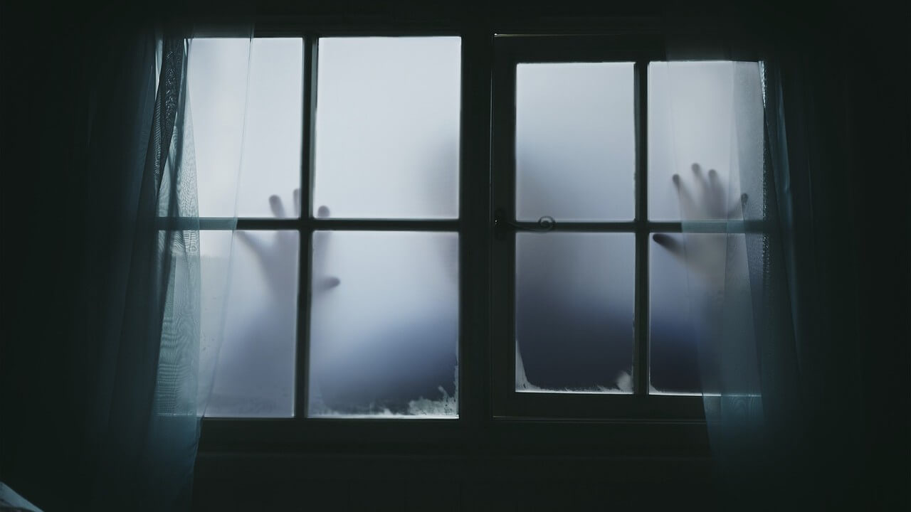 Scary photo of frosted windows with a dark shawdow of a person on the other side putting both hands on the glass