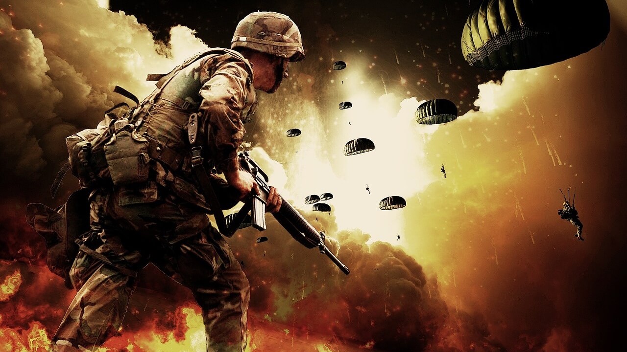 Picture of a soldier in battle, holding his gun with helicopters flying overhead dropping parachute soldiers