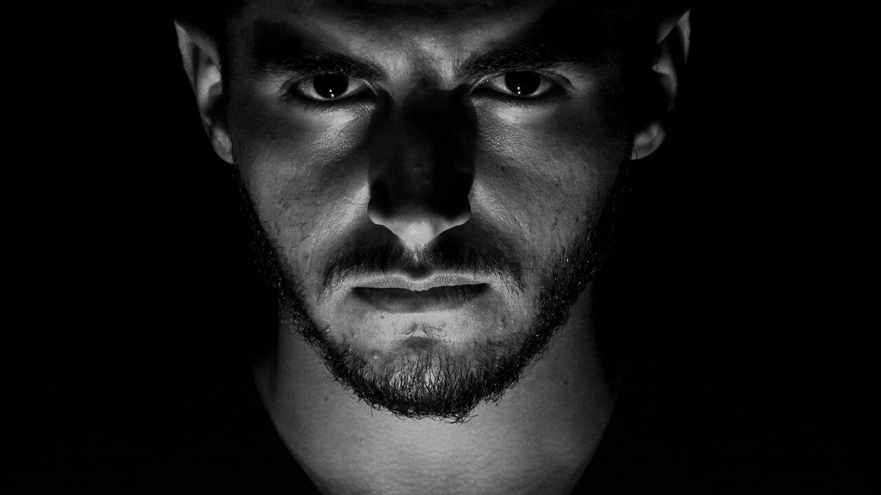 Face of a man with a black background, staring at the camera with furrowed brow.