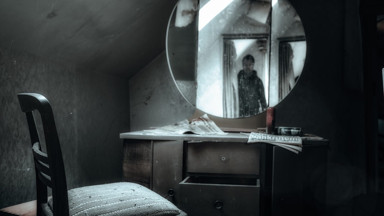 Man dressed in dark clothing, hiding in the doorway with his reflection in a mirror