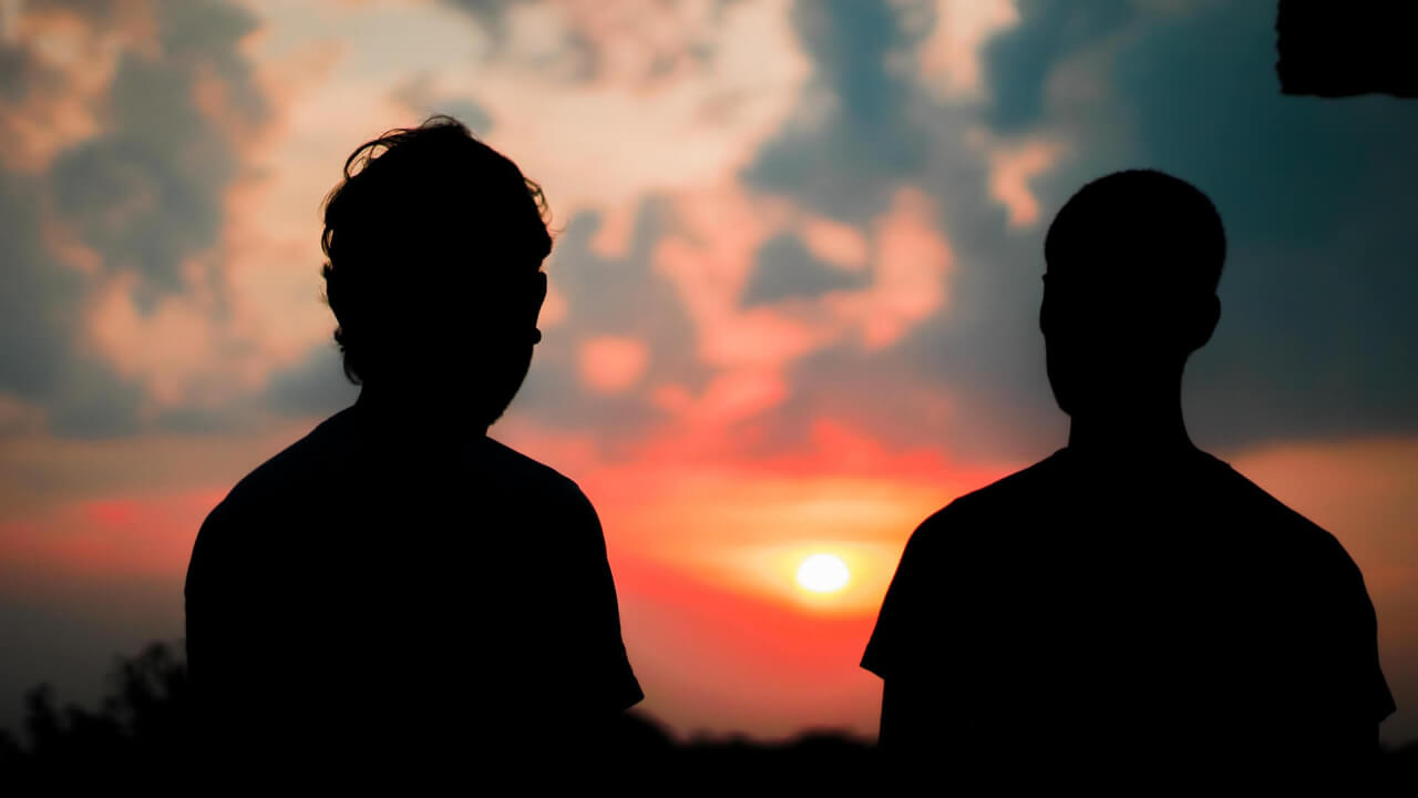 Two guys sitting side my side watching the sunset